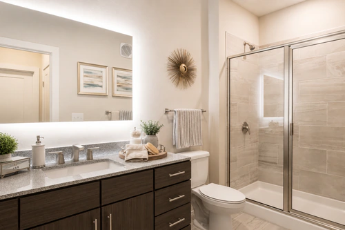 Bathroom with a granite vanity, backlit mirror, and glass walk in shower at The Mayfair Apartments