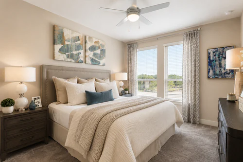 Bedroom with a ceiling fan, plush carpet, and a window overlooking the grounds at The Mayfair Apartments