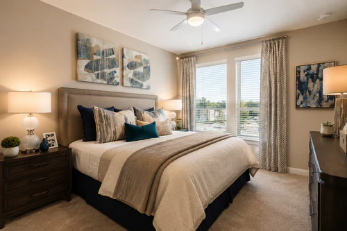 Carpeted bedroom with a ceiling fan and framed artwork at The Mayfair Apartments